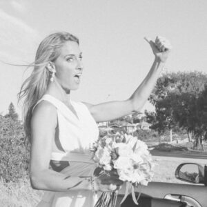 Bride hitch hiking with her thumb up and a flower bouquet