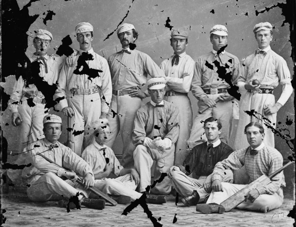Cricket team portrait before restoration, with large black losses and scratches across the players